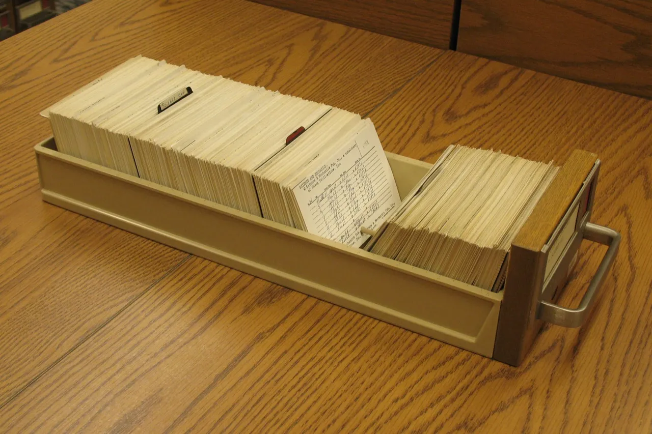 A long drawer of index cards on a wooden table, one typed card pulled up from the rest
